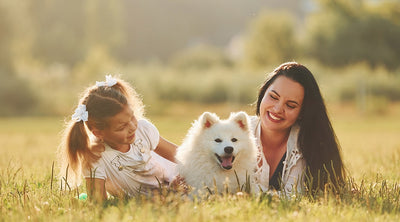 Smiling family with dog lying in grass on a sunny day, showing close contact that highlights pet parasite prevention and zoonotic transmission awareness.